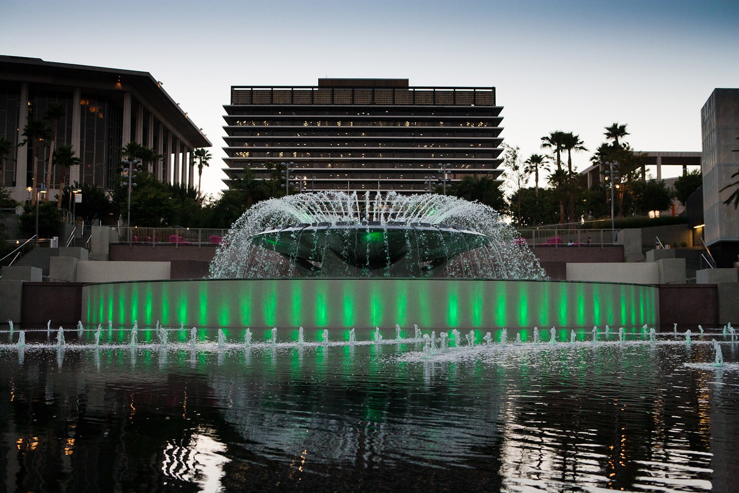 Image of water fountains with green lights and buildings in view